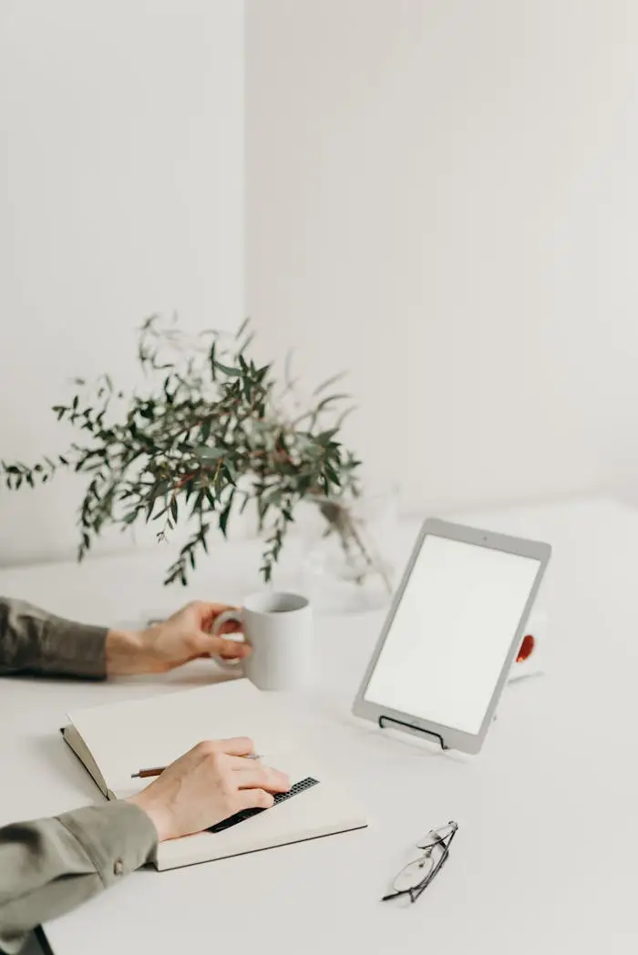 A minimalist home office setup with a blank screen tablet, coffee mug, and greenery.